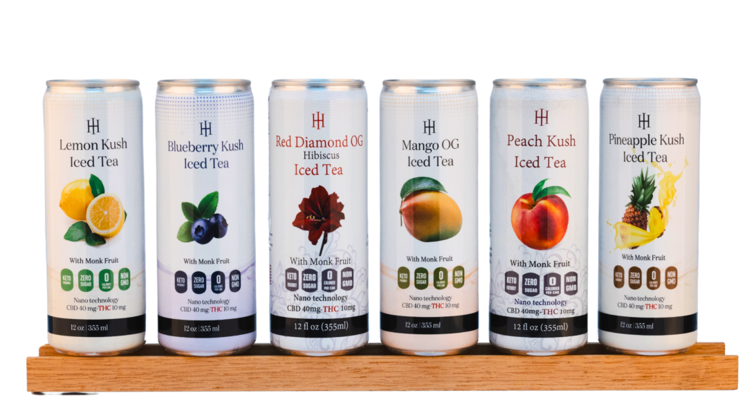 A lineup of The Specialty Club’s premium CBD and THC-infused iced tea beverages, featuring all flavors on display. Includes Mango OG, Blueberry Kush, Raspberry Kush, Peach Kush, Pineapple Kush, and Red Diamond OG Hibiscus, elegantly arranged on a wooden shelf.